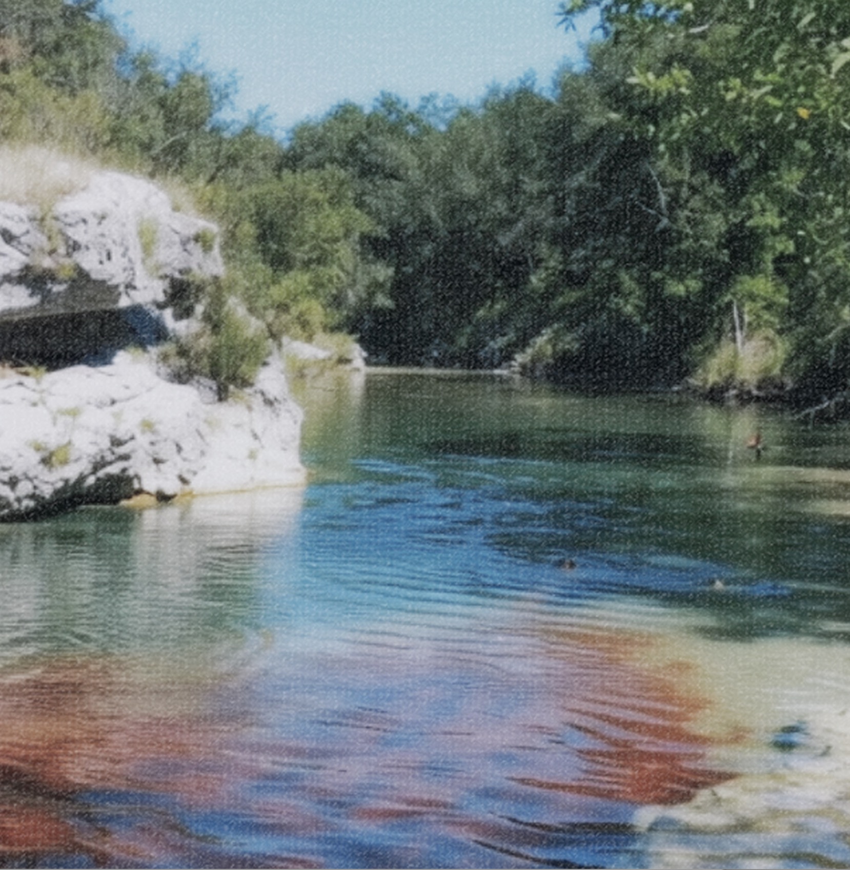 Clear spring-fed swimming hole ringed by limestone and trees