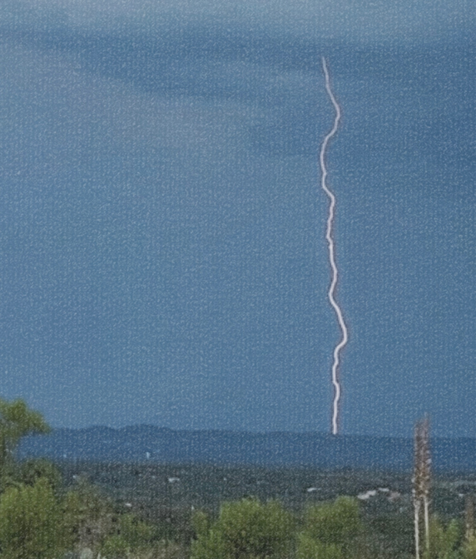 Lightning striking beyond the trees and distant Texas hills