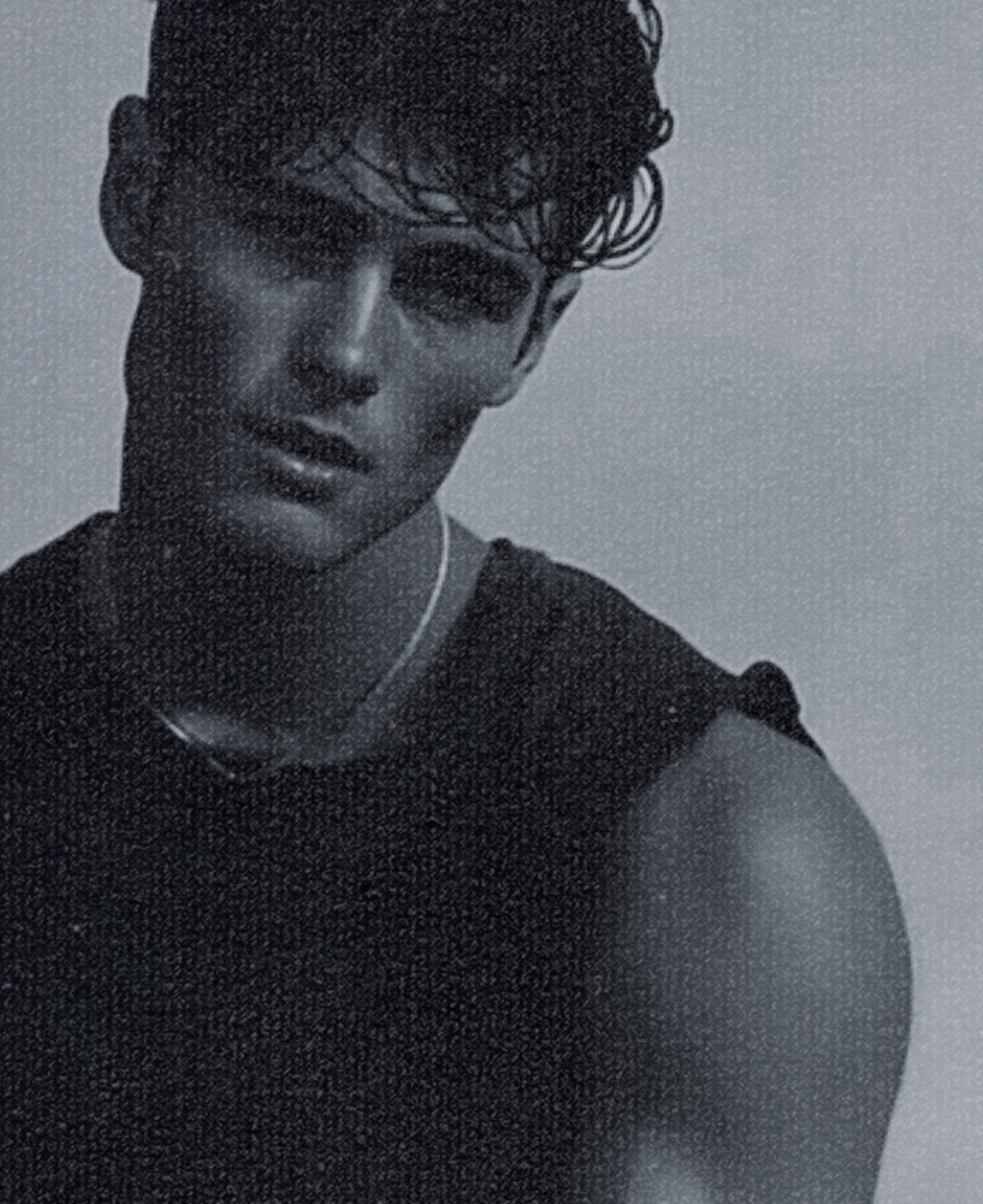 A young man with dark wavy hair wearing a dark sleeveless top