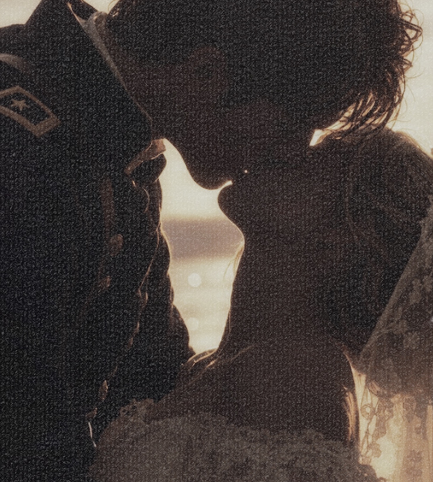 Silhouetted couple kissing against a golden seaside sky