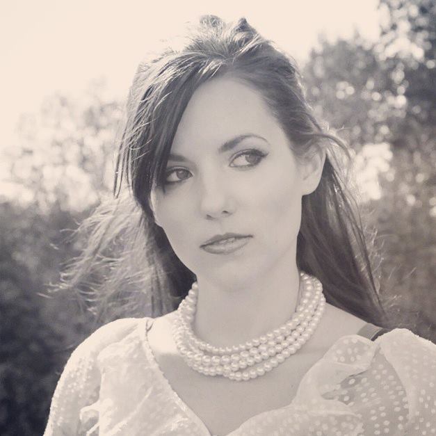 Portrait with swept-back hair and a pearl necklace, photographed outdoors